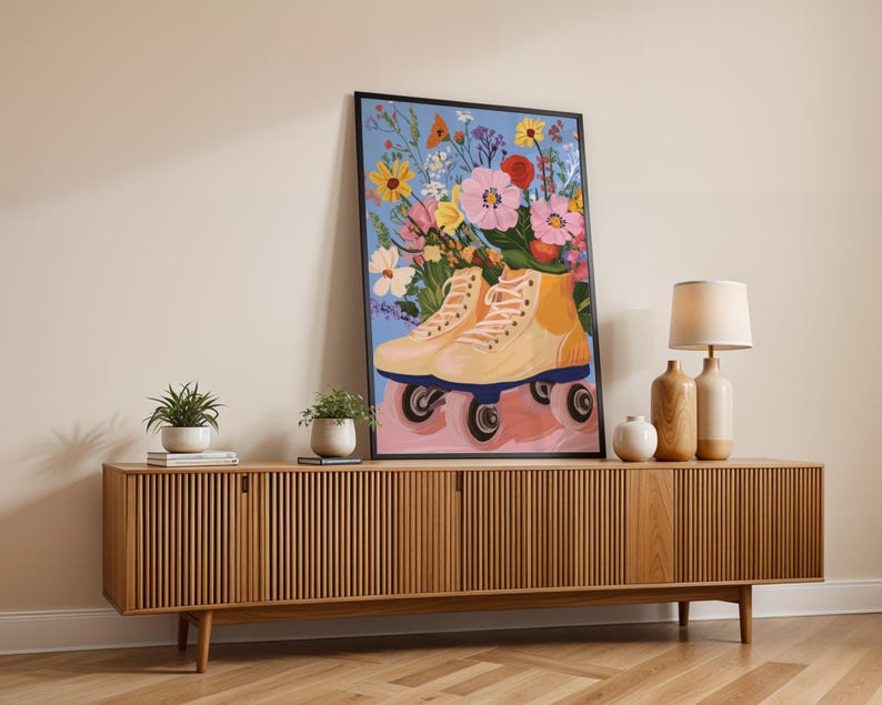 May include: A framed illustration of a pair of roller skates with a bouquet of colourful flowers in the skates. The background is a light blue colour. The roller skates are light yellow and have black wheels. The flowers are pink, yellow, orange, and purple. The illustration is hanging on a wall above a wooden cabinet.