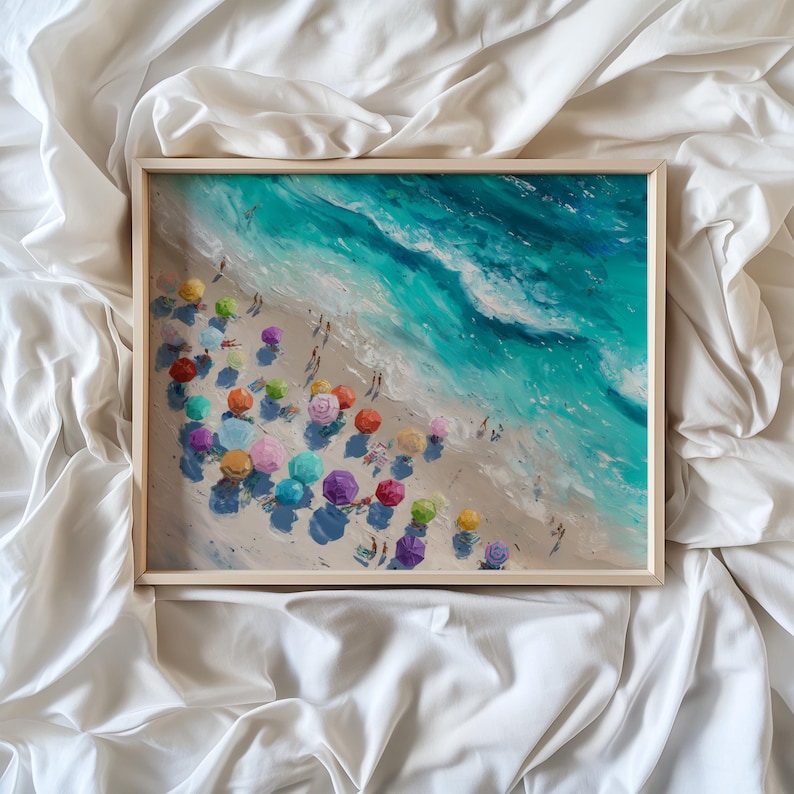 May include: A framed print of a beach scene with colourful parasols and turquoise waves. The painting shows people on the sand and the ocean. The artwork is in a light wooden frame.