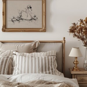 May include: A bedroom scene featuring a bed with beige and white striped pillows and bedding. Above the bed is a framed artwork with a sketch of a swan and cygnets. A gold-toned lamp sits on a wooden nightstand.