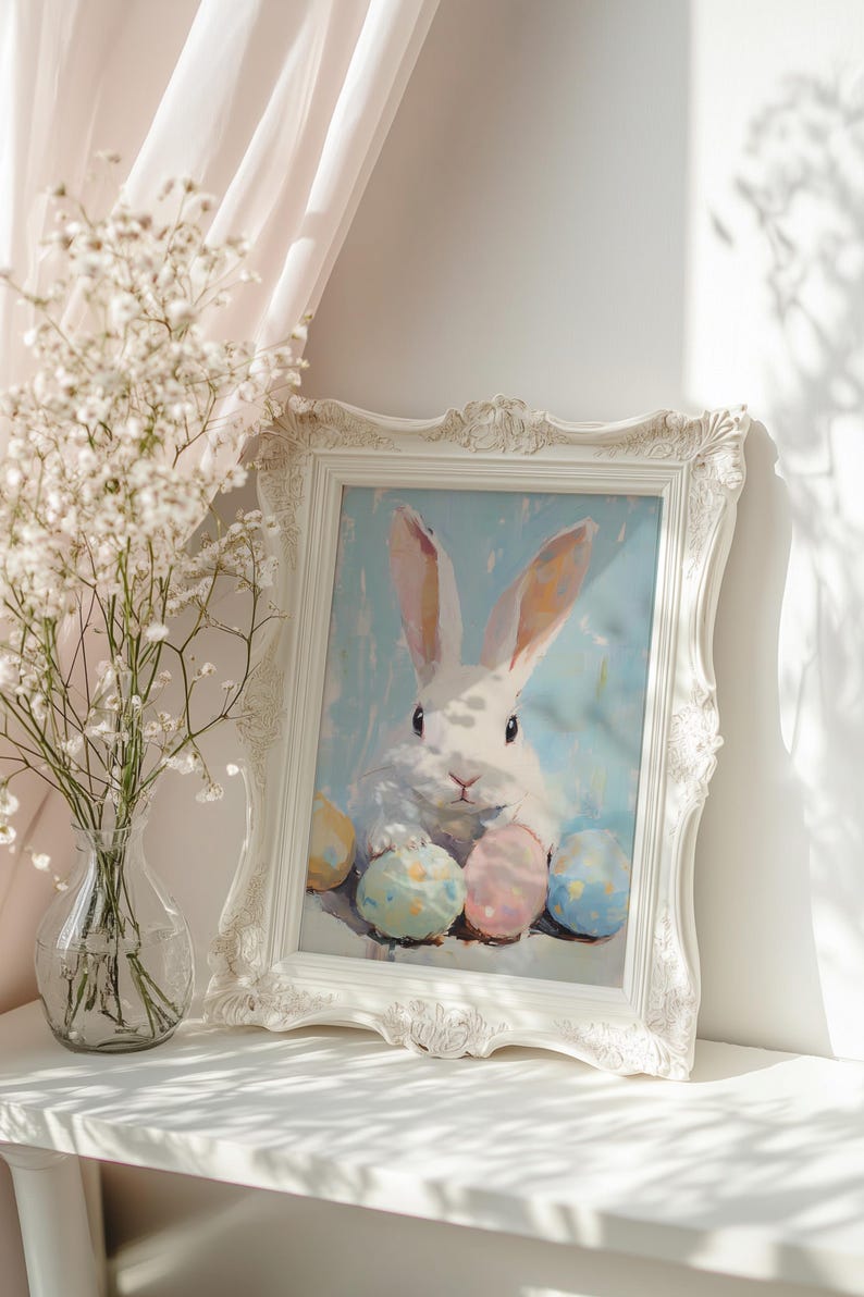 May include: A white rabbit with long ears sits surrounded by colorful Easter eggs in a white frame. The frame is on a white shelf with a vase of white flowers in the background.