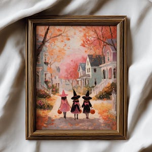 May include: A framed watercolor painting depicts three children in witch costumes walking down a street lined with houses. The children carry jack-o'-lantern buckets. The artwork has a warm color palette of orange, pink, and brown, evoking a fall or Halloween theme.