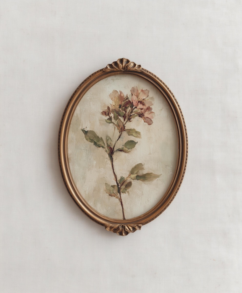 May include: An oval-shaped, antique-style framed floral painting. The artwork features a delicate sprig of pink and green flowers against a neutral background. The frame is a detailed gold color, adding to the vintage aesthetic.