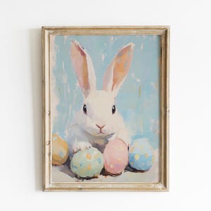 May include: A white rabbit with pink ears sits surrounded by colorful Easter eggs. The rabbit is looking directly at the viewer. The background is a light blue.