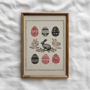 May include: Framed Easter art print featuring a gray rabbit surrounded by floral elements and six decorated eggs in red and black. The artwork is set against a cream background and framed in gold.
