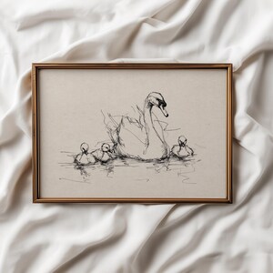 May include: A framed pen and ink drawing of a swan and cygnets. The artwork features a mother swan with three cygnets swimming in the water. The frame is a gold color and the background is a neutral beige.