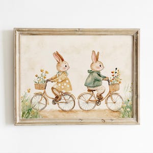 May include: Two watercolor bunnies riding bicycles with baskets of flowers. The bunny on the left is wearing a yellow polka dot dress and the bunny on the right is wearing a green jacket. The background is a light brown.