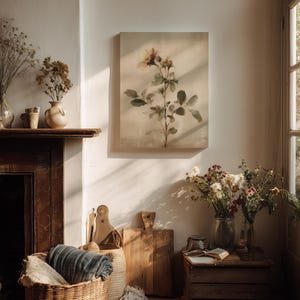 Puede incluir: Un interior acogedor con una pintura floral, una cesta de mimbre con una manta y tablas de cortar de madera. Flores secas en jarrones y una peque&ntilde;a caja de madera con un libro completan la escena. La pintura representa una rosa con hojas verdes.