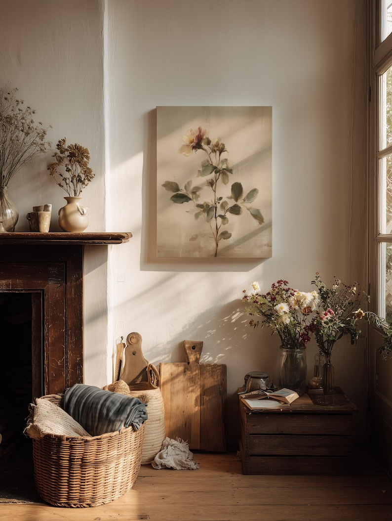 Puede incluir: Un interior acogedor con una pintura floral, una cesta de mimbre con una manta y tablas de cortar de madera. Flores secas en jarrones y una peque&ntilde;a caja de madera con un libro completan la escena. La pintura representa una rosa con hojas verdes.