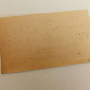 Puede incluir: Un trozo rectangular de papel envejecido, de color marr&oacute;n claro, con texto descolorido. El papel tiene un borde ligeramente curvado y parece ser vintage. El texto es dif&iacute;cil de leer, lo que sugiere que podr&iacute;a ser un documento o una nota antigua.