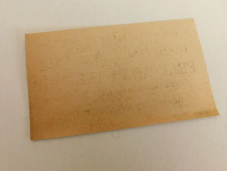 Puede incluir: Un trozo rectangular de papel envejecido, de color marr&oacute;n claro, con texto descolorido. El papel tiene un borde ligeramente curvado y parece ser vintage. El texto es dif&iacute;cil de leer, lo que sugiere que podr&iacute;a ser un documento o una nota antigua.