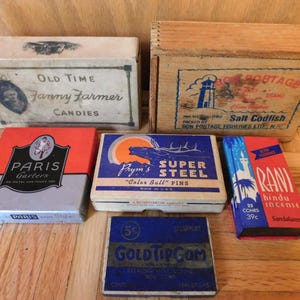 May include: A collection of vintage boxes and packaging, including a candy box, a salt codfish box, and boxes for garters, pins, gum, and incense. The boxes feature various colors and graphics, with text such as "Old Time Fanny Farmer Candies" and "Paris Garters."