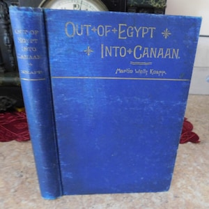 May include: A blue hardcover book with gold lettering on the cover. The title is "Out of Egypt Into Canaan" by Martin Wells Knapp.