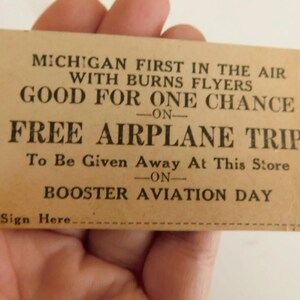 Puede incluir: Una tarjeta vintage de color beige con texto negro. La tarjeta dice "MICHIGAN FIRST IN THE AIR WITH BURNS FLYERS GOOD FOR ONE CHANCE ON FREE AIRPLANE TRIP." La tarjeta es para el Booster Aviation Day.