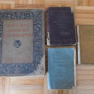 May include: Four vintage hardcover books with different titles and designs. The books are brown, blue, purple, and tan. The book on the left has a floral design and the text "Natural Advanced Geography".