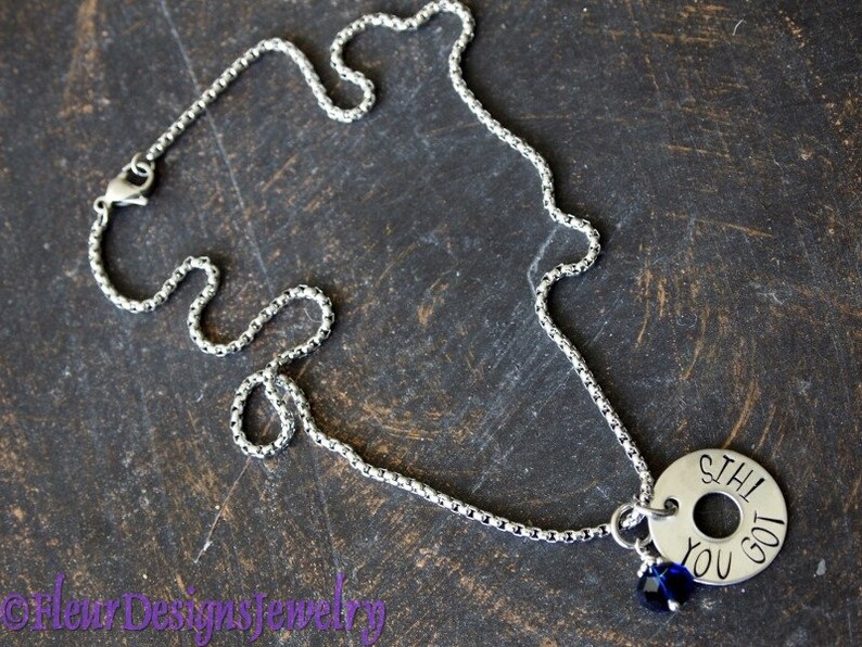 May include: A silver chain necklace with a silver charm that reads "Still You Got" and a small blue crystal charm.