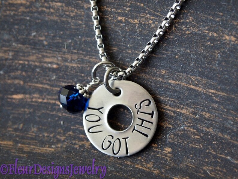 May include: Silver necklace with a round charm that says "You got this" and a dark blue crystal bead.