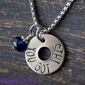 May include: A silver necklace with a round charm that says "You got this". The charm has a small blue crystal attached to it.