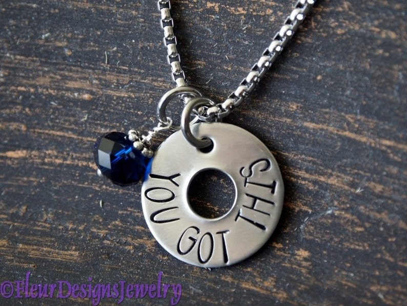 May include: A silver necklace with a round charm that says "You got this". The charm has a small blue crystal attached to it.