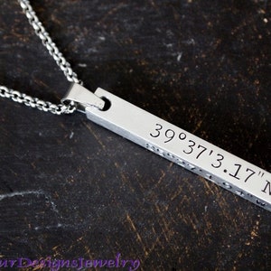 May include: Silver necklace with a bar pendant engraved with the coordinates 39°37'3.17" N.