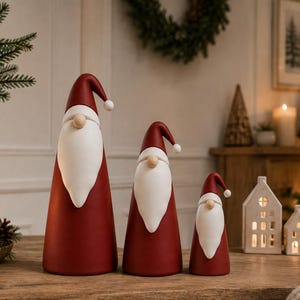 May include: Three cone-shaped Santa figurines in varying sizes, each featuring a deep red body, a long white beard, a round beige nose, and a matching red pointed hat with a small white pom-pom at the tip, arranged in a row on a wooden surface.