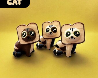 May include: Three brown and white cat figurines wearing toast-shaped hats. The cats have large eyes and are sitting on a yellow surface. The text "Toast CAT" is in the top left corner of the image. The text "Mini Figure" is in the bottom centre of the image.