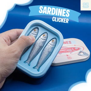 May include: A light blue sardine-shaped clicker toy with three silver fish inside. The toy is held in a hand, with a sardine can lid visible. The text "Sardines Clicker" is displayed on a blue banner.