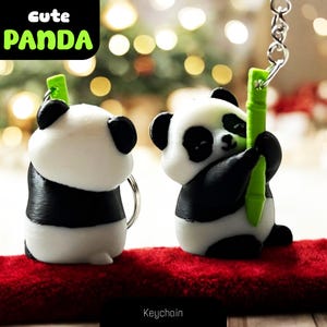 May include: Two panda bear keychains, one black and white panda holding a green bamboo stick, the other black and white panda standing on its hind legs. The keychains are on a red velvet surface. The text "Cute Panda" is in the top left corner of the image. The text "Keychain" is in the bottom centre of the image.