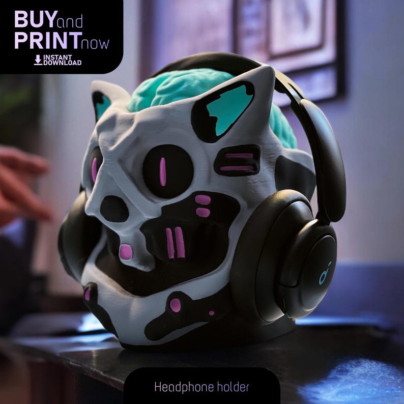 May include: A 3D printed headphone holder shaped like a cat's head with a brain inside. The cat's head is white with black and pink details. The headphones are black with a blue accent.