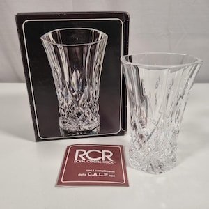 Könnte beinhalten: Eine klare Kristallvase mit einem rautenförmigen Muster auf der unteren Hälfte und einem glatten, geschwungenen Design auf der oberen Hälfte. Die Vase wird neben ihrer originalen schwarzen Schachtel und einer kleinen Karte mit dem Text "RCR ROYAL CRYSTAL ROCK" präsentiert.