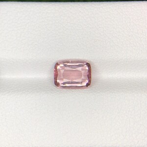 May include: A rectangular, light pink gemstone with rounded corners. The gem is set against a white background, showcasing its color and clarity. The stone appears to be faceted, reflecting light. The overall presentation suggests a precious stone.