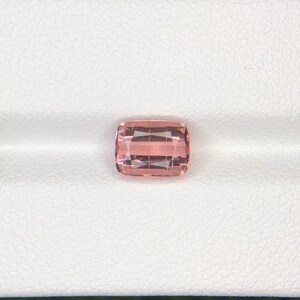 May include: A cushion-cut, light pink gemstone. The gem is set against a white background, showcasing its facets and color. The stone appears to be a high-quality, polished jewel, suitable for jewelry.