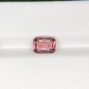 May include: A rectangular, faceted gemstone with rounded corners, exhibiting a soft pink hue. The gem is set against a white background, highlighting its color and clarity. The stone's facets catch the light, creating a subtle sparkle. This gemstone is likely for jewelry.