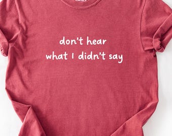 May include: A red t-shirt with the phrase "don't hear what I didn't say" printed in white. The shirt has a crew neck and short sleeves, with the sleeves rolled up. The fabric appears soft and slightly faded.