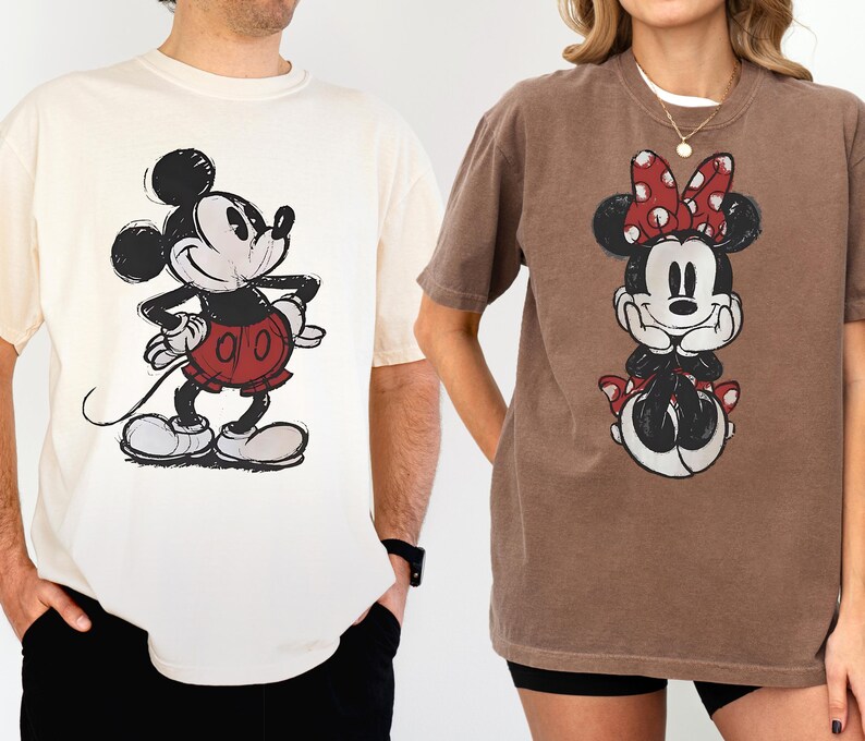 以下が含まれることがあります： ディズニーキャラクターが描かれたTシャツ2枚。1枚はクリーム色で、ミッキーマウスのグラフィックが黒、赤、白で描かれています。もう1枚は茶色で、ミニーマウスのグラフィックが黒、赤、白で描かれています。どちらのシャツも半袖です。