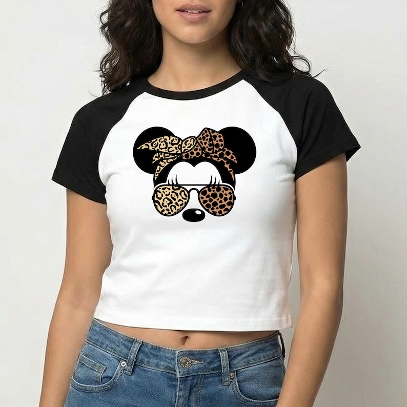 Op de afbeelding: Witte crop top met zwarte raglanmouwen met een afbeelding van een muis met een luipaardprint strik, zonnebril en oren. De muisafbeelding heeft een zwarte neus en draagt een zonnebril met luipaardprint.