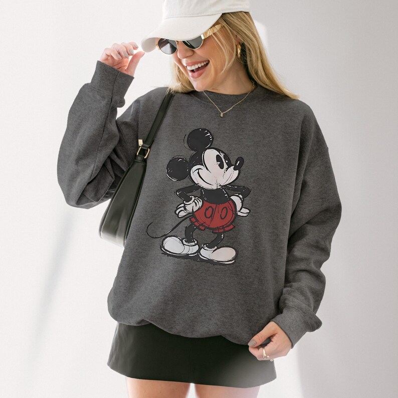 May include: Dark gray sweatshirt featuring a distressed graphic of Mickey Mouse. The cartoon character is depicted in black, white, and red. The sweatshirt has a crew neck and long sleeves.