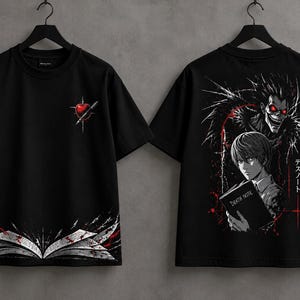 May include: A black t-shirt featuring a front graphic of a red apple pierced by a pen and an open book at the hem. The back displays a graphic of a character holding a book titled Death Note, with a creature above and Japanese text.
