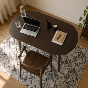 Peut inclure: Un bureau ovale en bois brun foncé avec quatre pieds fuselés, accompagné d'une chaise en bois assortie. La surface du bureau comprend un ordinateur portable argenté, un verre d'eau, une bouteille en verre avec bouchon, un pot à crayons, une bougie et un carnet.