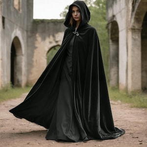 May include: A black velvet hooded cape with a silver clasp. The cape is worn by a person standing in front of a stone archway.