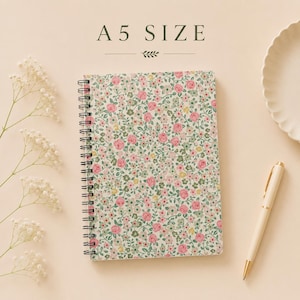 May include: An A5 size spiral-bound notebook featuring a dense floral pattern of pink roses and small green leaves on a cream background. The notebook is positioned next to a cream-colored pen and delicate white baby's breath flowers.