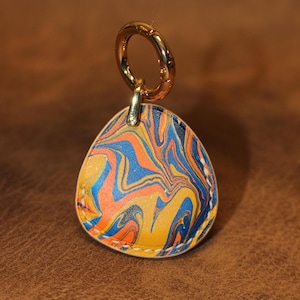 May include: A colourful leather keychain with a marbled pattern in shades of blue, orange, and yellow. The keychain has a gold metal ring.