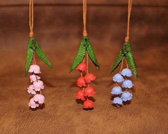 May include: Three leather lily of the valley charms with green leaves and different colored flowers: pink, red, and blue.