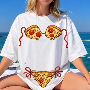 Könnte beinhalten: Weißes T-Shirt mit einem Bikini-Design aus Pizzastücken. Die Pizzastücke haben Beläge aus Peperoni und Pilzen. Das T-Shirt wird auf einem Boot mit blauem Ozeanhintergrund getragen.