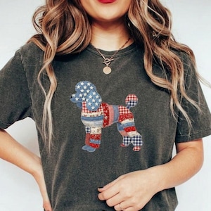 Könnte beinhalten: Dunkelgraues T-Shirt mit einem Patchwork-Pudel-Design in Rot, Weiß und Blau. Der Kopf des Pudels ist blau mit weißen Sternen, und sein Körper ist eine Mischung aus karierten und gestreiften Mustern. Das Shirt hat kurze Ärmel und einen Rundhalsausschnitt.