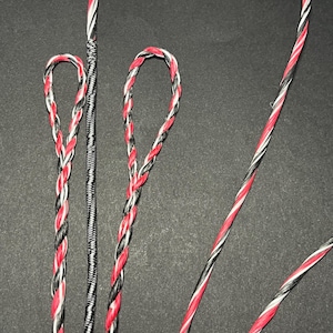Może przedstawiać: Zbliżenie kilku cięciw w kolorze czerwonym, czarnym i białym. Sznurki są zaplecione i zapętlone na końcach. Jeden sznurek ma jednolity czarno-biały wzór. Tło jest jednolicie czarne.