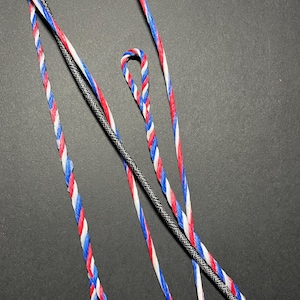 Może przedstawiać: Trzy sznurki do łucznictwa, jeden czarny i szary, a dwa czerwone, białe i niebieskie.