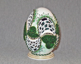 A cut, painted and beaded goose egg on a corian stand.