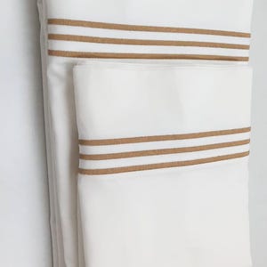 May include: Two white pillowcases with brown stripes. The pillowcases are folded and stacked on top of each other.