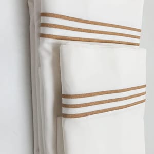 Puede incluir: Ropa de cama blanca con ribete marrón. La ropa de cama está doblada en una pila.