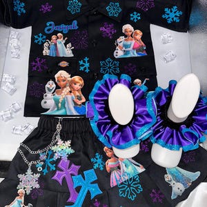 Könnte beinhalten: Schwarzes Outfit-Set mit einem Hemd mit Knöpfen und einem plissierten Rock, verziert mit Schneeflocken- und Charaktergrafiken. Das Set enthält passende Scrunchies. Das Hemd hat den Namen "Jasiyah" aufgestickt. Das Outfit ist mit lila und blauen Akzenten verziert.